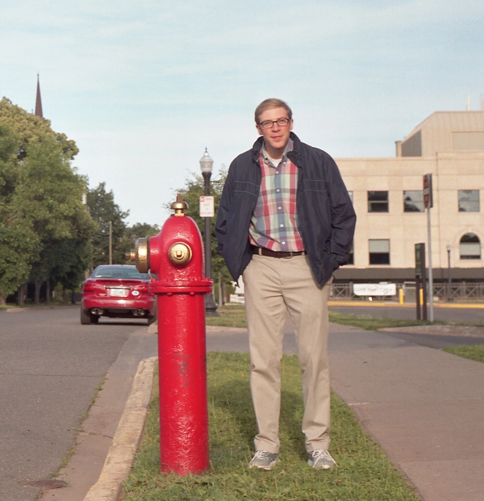 Joe Pera, a white man with glasses standing next to a red fire hydrant.